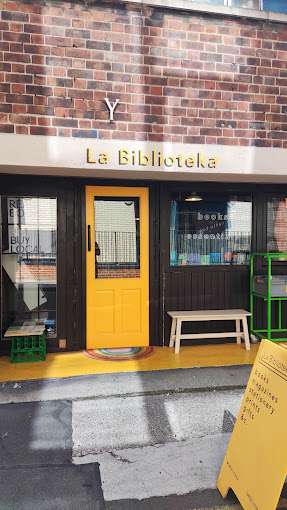 Exterior view of La Biblioteka, showing its distinctive yellow door and sign.