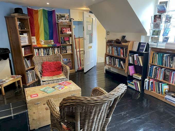 The interior of the People's Bookshop in Durham, showcasing shelves filled with books, a rainbow flag on the wall, and comfortable chairs around a wooden table. The warm space and an inviting atmosphere. © People's Bookshop Durham