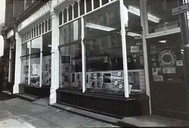 A black and white photo of the Mushroom Bookshop's exterior, showing large display windows and the entrance door with signage.